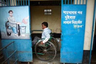 A disabled man uses the accessible latrine designed specifically to accommodate his needs, Beltola slum, Dhaka, Bangladesh